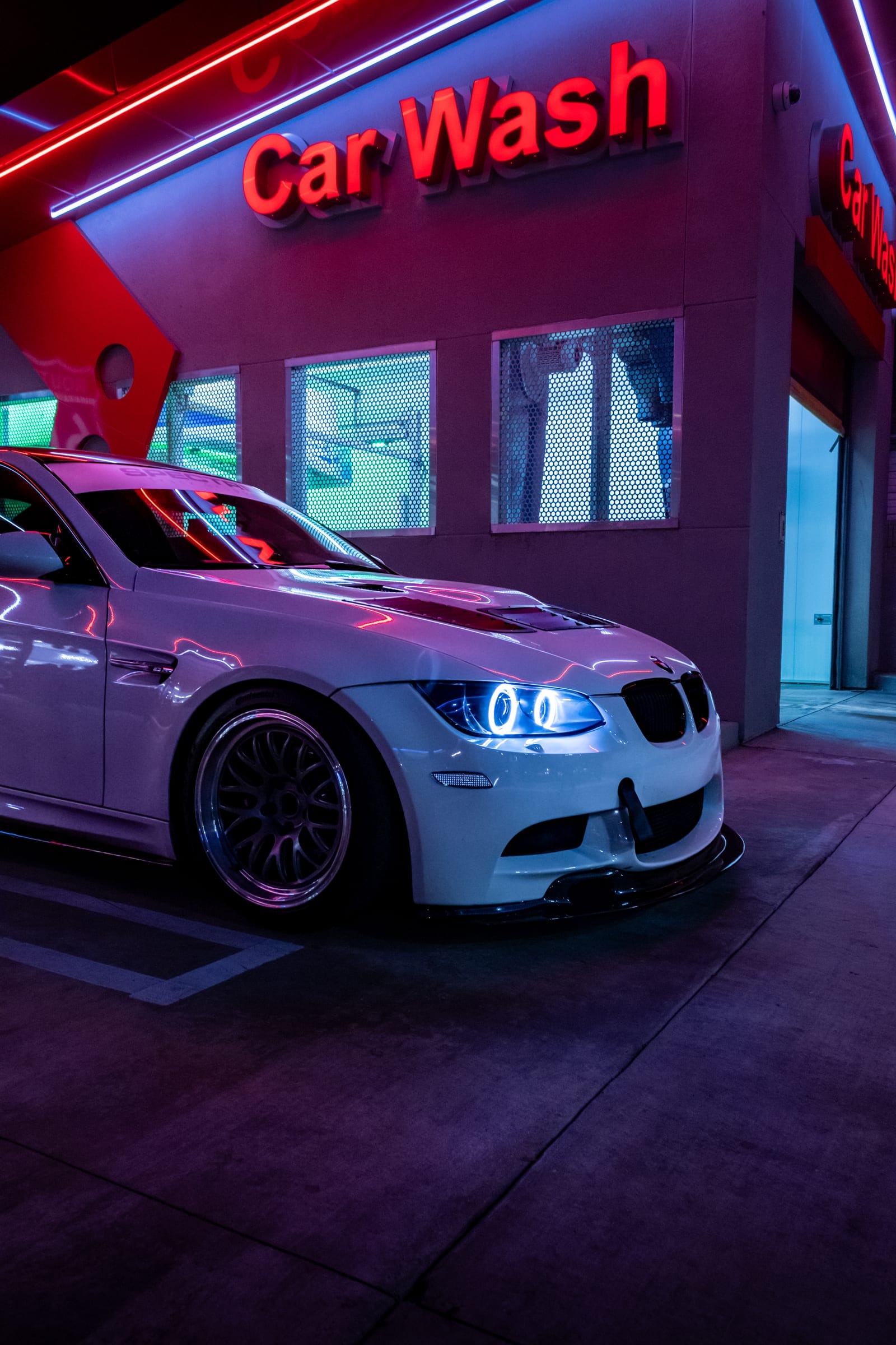 A white BMW M3, angel eyes lit, under the Car Wash neon sign